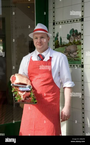 butcher-standing-in-shop-doorway-wearing-red-apron-w-irvine-butchers-AXKJYW.webp